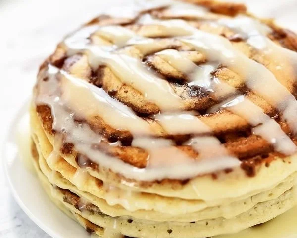 Stack of cinnamon roll pancakes drizzled with icing and topped with cinnamon sugar