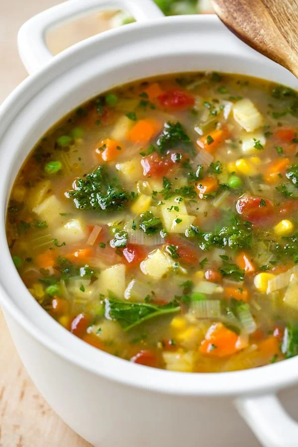 A bowl of colorful vegetable soup filled with fresh vegetables and herbs.